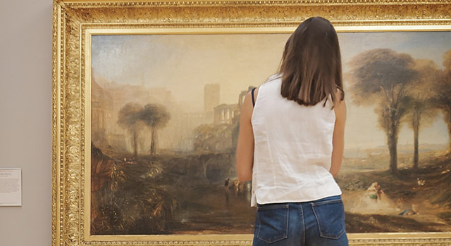 ターナーの風景画を閲覧する女性の後ろ姿