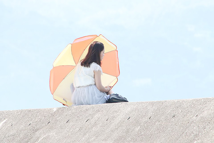 防波堤で外洋に向かい座り日傘をさした女性
